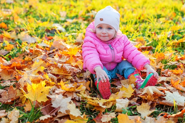 Happy young girl playing under falling yellow leaves in beautiful autumn park