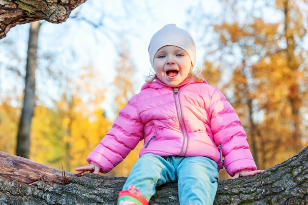 Happy young girl smiling and sitting on tree in beautiful autumn park