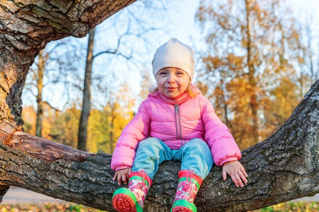 Happy young girl smiling and sitting on tree in beautiful autumn park