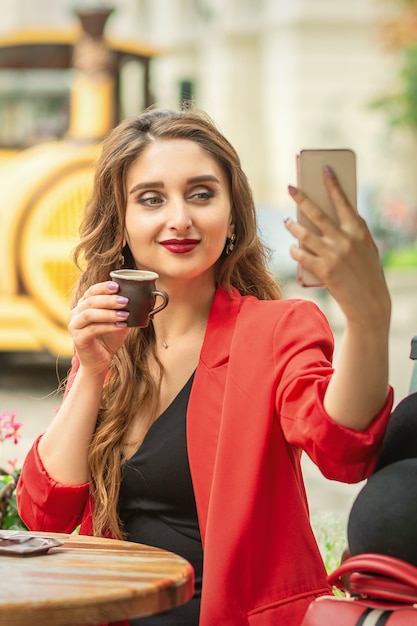 Happy young girl taking selfie at cafe outdoors.