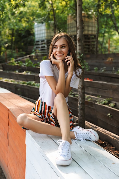 Happy young girl talking on mobile phone at the park outdoors