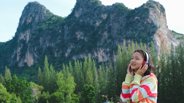 Happy young girl wear sweater listening music sitting on beautiful landscape view.