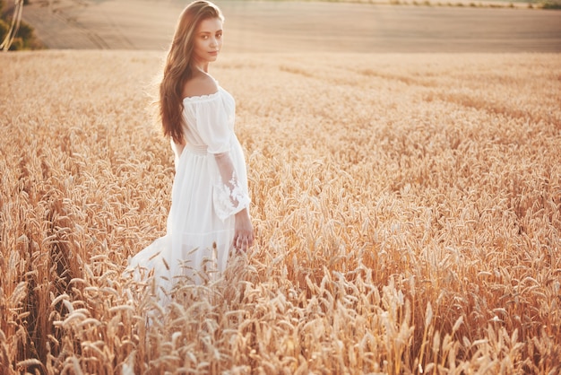 Happy young girl with long, beautiful hair standing in a wheat field under the sunlight