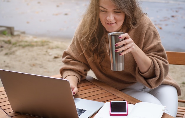 Happy young girl working at a coffee shop with a laptop