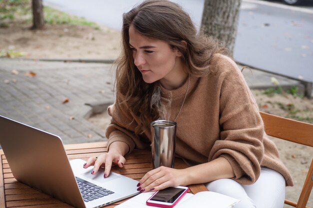 Happy young girl working at a coffee shop with a laptop