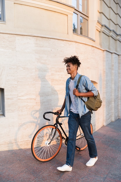 Happy young guy walking with bicycle outdoors on the street