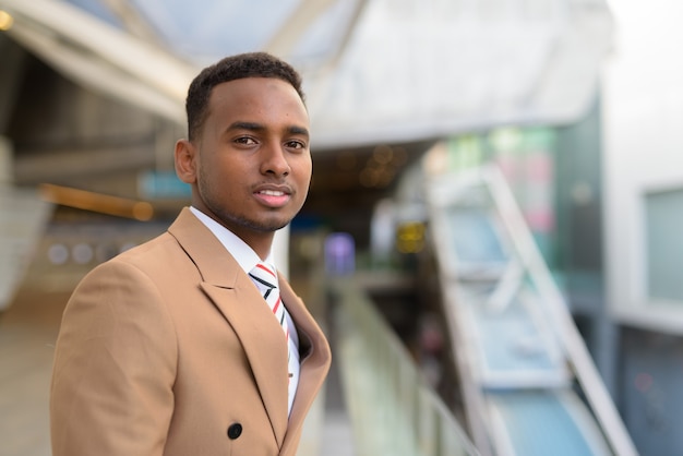 Happy young handsome African businessman at footbridge in the city