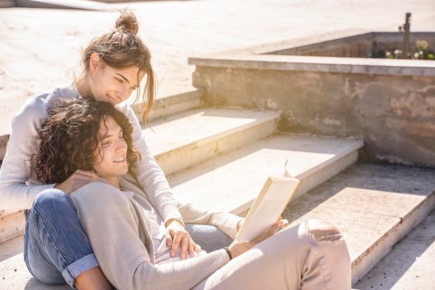 Happy young heterosexual couple smiling and reading book outdoor