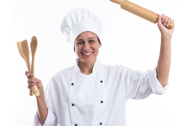 Happy young hispanic girl in cook's uniform holding kitchenware isolated on a white background