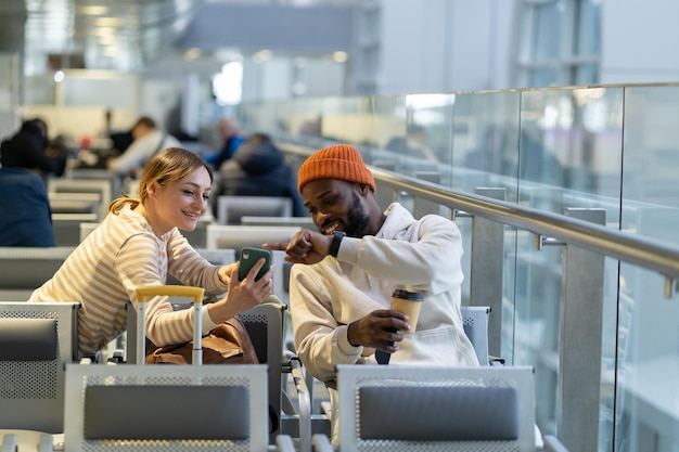 Happy young international couple sitting in airport lounge talking to each other waiting departure