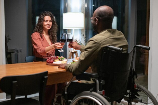 Happy young interracial couple sitting by festive table and toasting