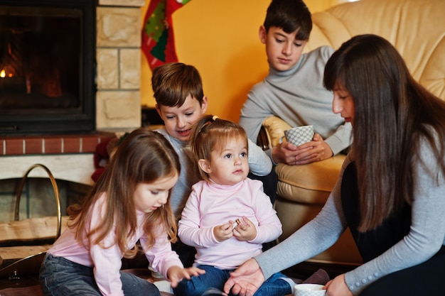 Happy young large family by a fireplace in warm living room on winter day Mother with four kids at home read book