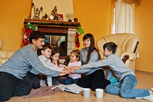 Happy young large family at home by a fireplace in warm living room on winter day Hand on hands