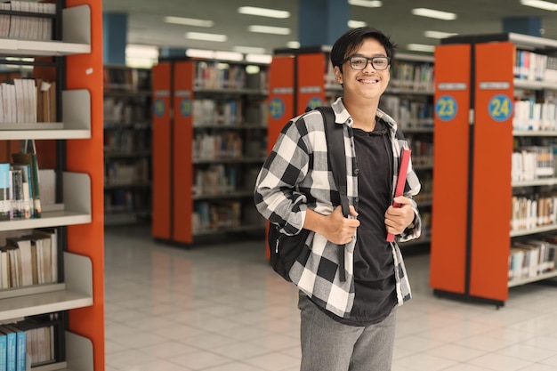 Happy young male student standing on public library for work on study research project