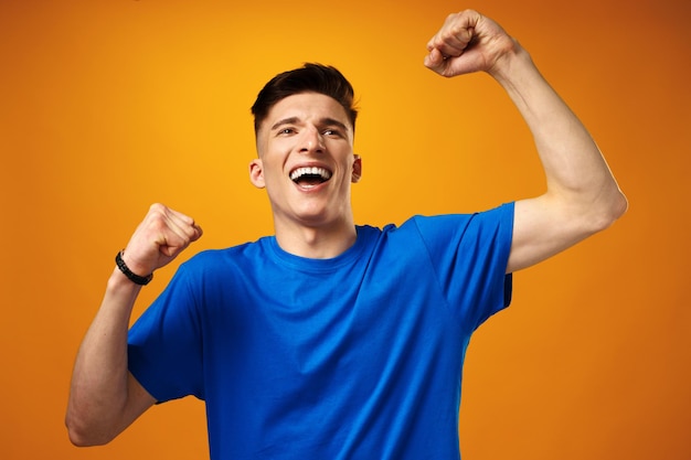 Happy young man in blue tshirt smiling with raised hands celebrating success