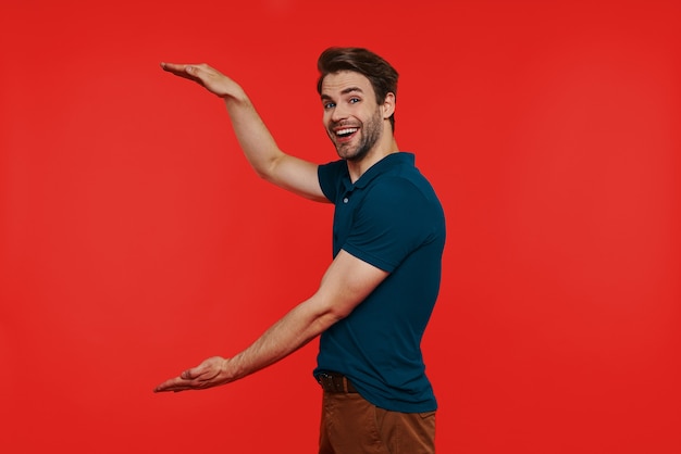 Happy young man in casual wear and gesturing while standing against red wall