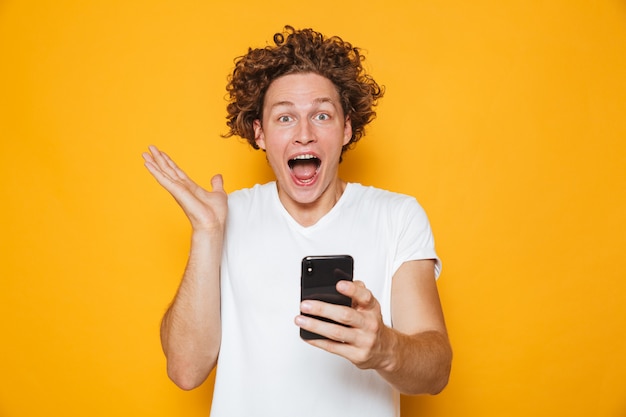 Happy young man in casual white t-shirt screaming while holding smartphone