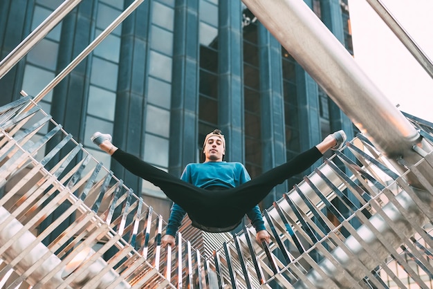 Photo happy young man doing acrobatic poses in a metal sculpture