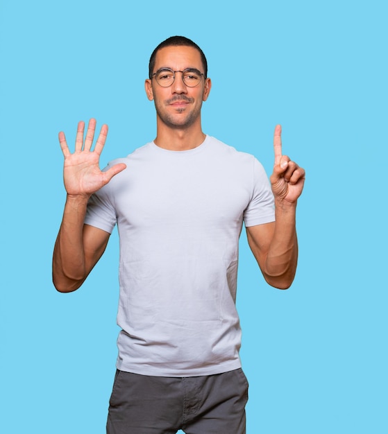 Happy young man doing a number six gesture with his hands