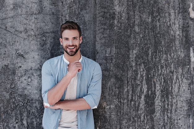 Happy young man dressed casually in blue stylish shirt and grey T-shirt, having a decisive attitude, smiling and looking at camera, isolated over grey background. Success concept