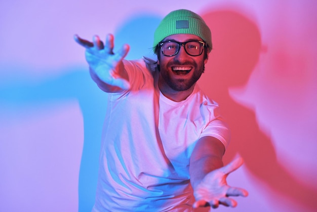 Happy young man in funky hat stretching out hands while standing against colorful background