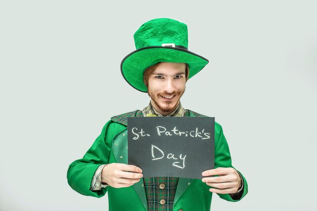 Happy young man in green suit holding dark tablet with written words St. Patrick's day.