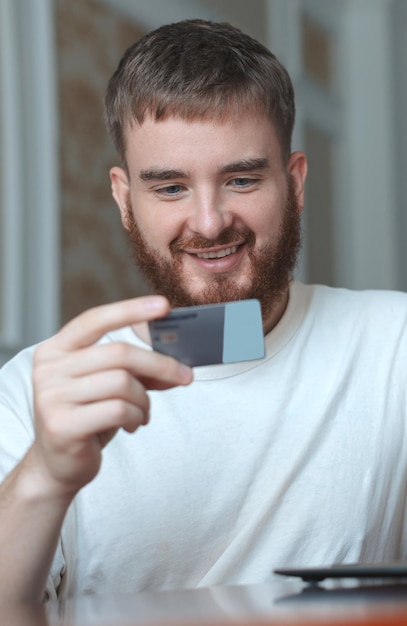 Happy young man hold credit bank card in hand use laptop computer smile at home shopping online