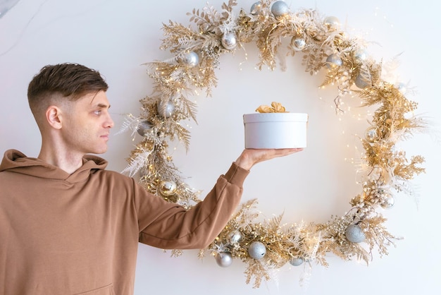 Happy young man holding gift box on background Christmas wreath on background