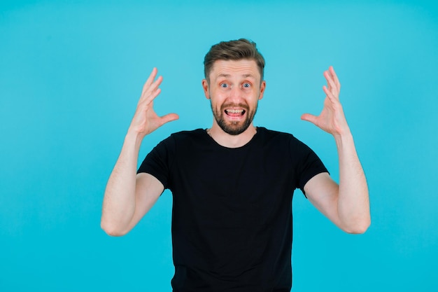 Happy young man is raising up his hands on blue background