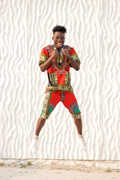 Happy young man jumping in Nigerian national clothes on a white wall