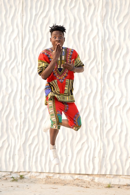 Happy young man jumping in Nigerian national clothes on a white wall