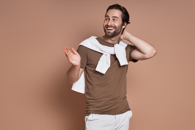 Happy young man looking away and gesturing against brown background