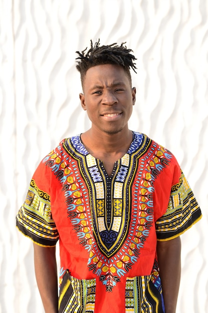 Happy young man in Nigerian national clothes on a white wall