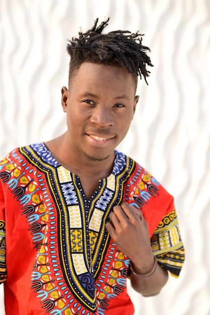 Happy young man in Nigerian national clothes on a white wall