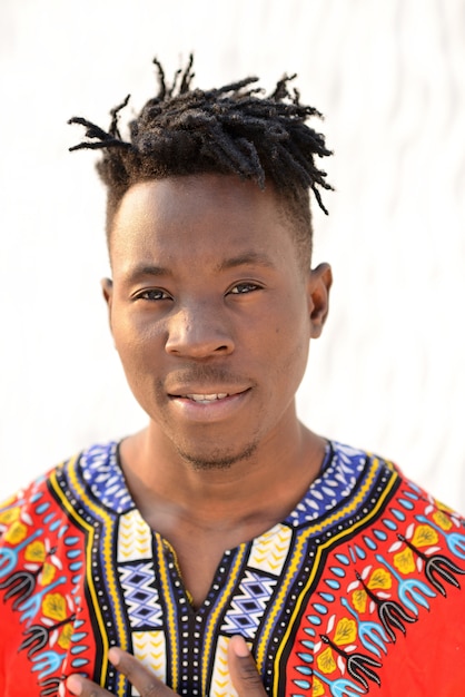 Happy young man in Nigerian national clothes on a white wall