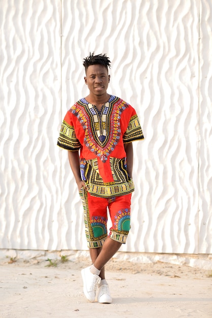 Happy young man in Nigerian national clothes on a white wall