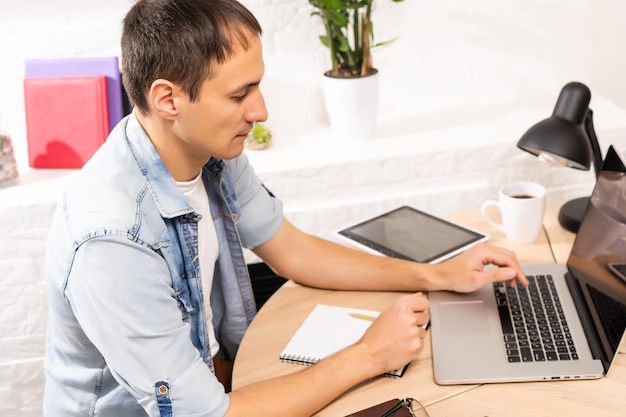 Happy young man smiling, as he works on his laptop to get all his business done early in the morning with his cup of coffee