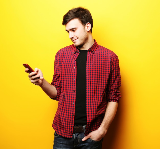 Happy young man talking on cell phone over yellow background