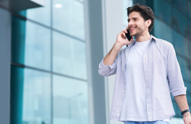 Happy Young Man Talking On Cellphone While Walking Near Airport Terminal