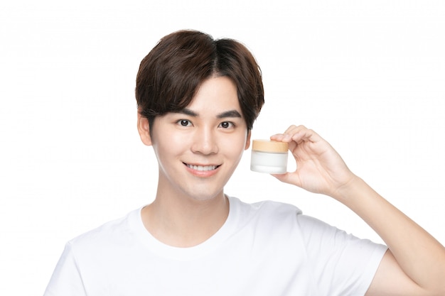 Happy young man using cream on his face against white wall