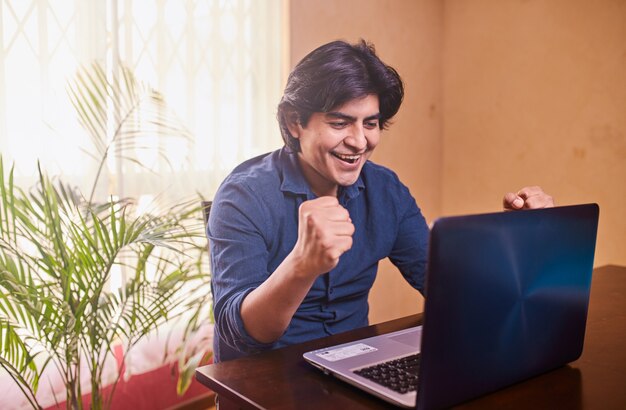 Happy young man using laptop or computer at desk.