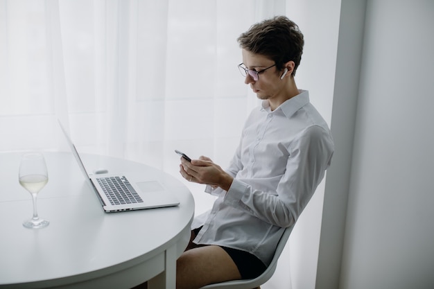 Happy young man, wearing glasses and smiling, as he works on his laptop. Man in quarantine works at home. Stay at home.