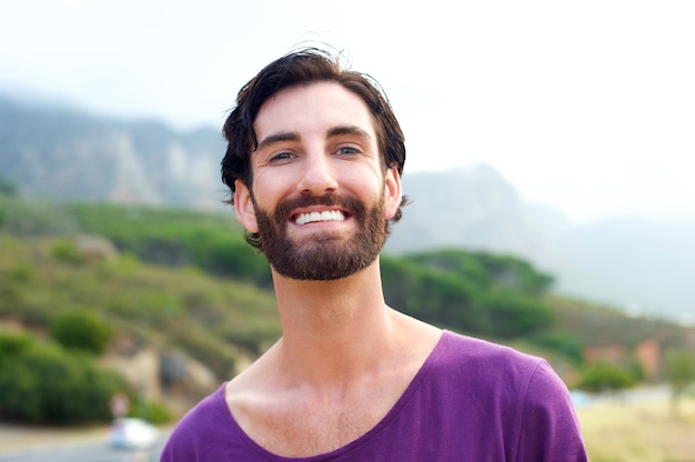 Happy young man with beard smiling outdoors