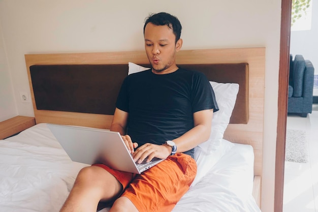 Happy young man working from the bed Put the laptop on the bed and type on the keyboard