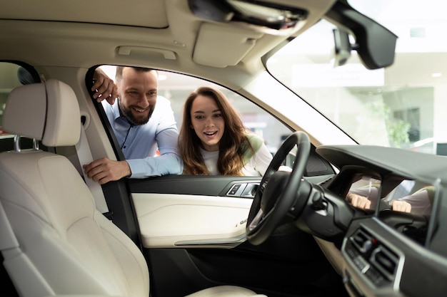 Happy young married couple looks into the interior of a new car