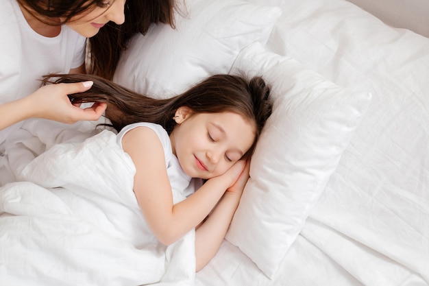 Happy young mother hugs her little daughter in bed