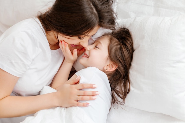 Happy young mother hugs her little daughter in bed