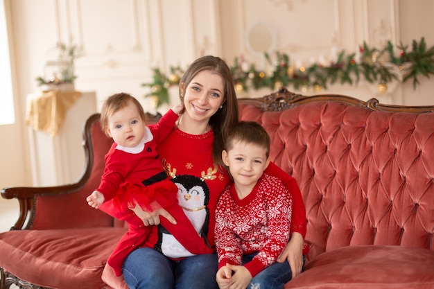 Happy young mother hugs her sons on sofa near Christmas tree