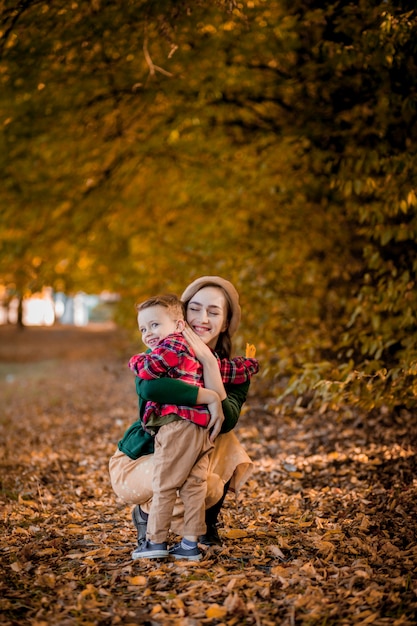 Happy young mother playing and having fun with her little baby son on warm autumn day in the park