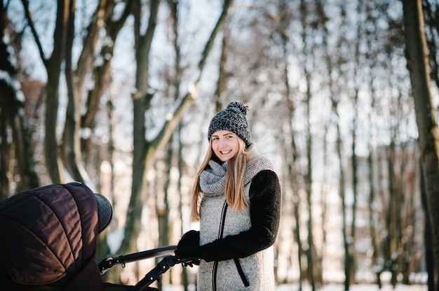 A happy young mother walks with a stroller and baby in a winter park